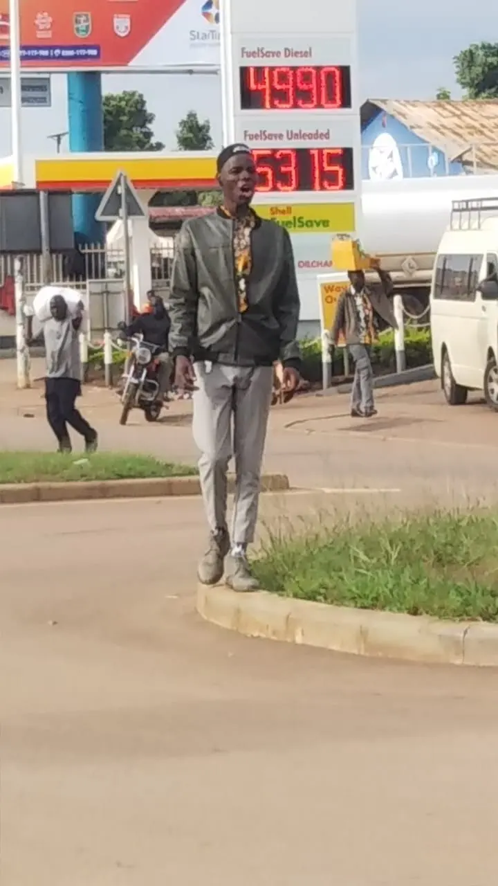Young evangelist preaching aloud beside a busy fuel station on a town road